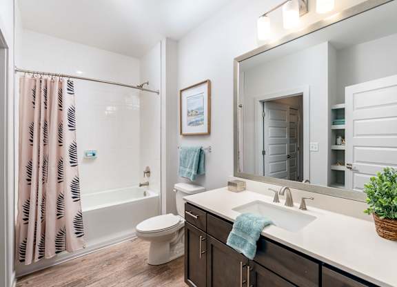 A bathroom with a white sink, toilet, and a shower with a pink shower curtain.