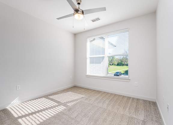 A room with a ceiling fan and a window showing a view of a house and trees outside.