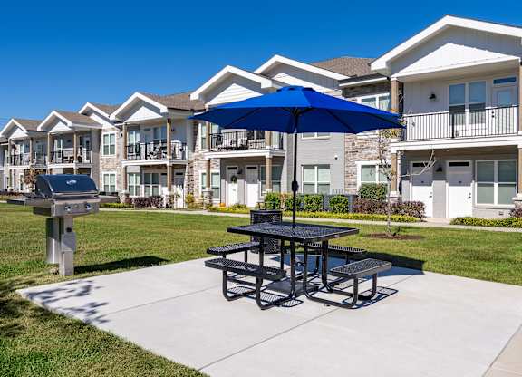 A picnic table with a blue umbrella is in the foreground of a residential area.