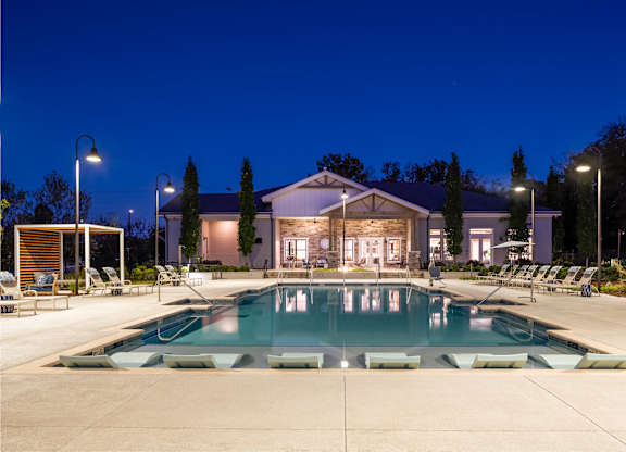 A large swimming pool in front of a building with lounge chairs around it.