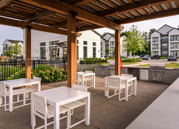 A patio with white chairs and tables under a wooden pergola.