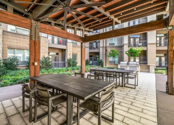 a patio with wooden tables and chairs and an apartment building in the background