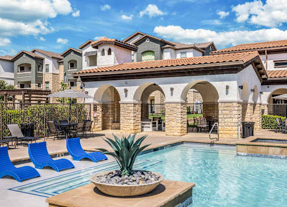 A pool area with a stone archway and blue lounge chairs.