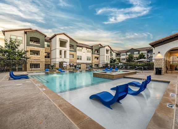 A swimming pool with blue loungers in front of apartment buildings.