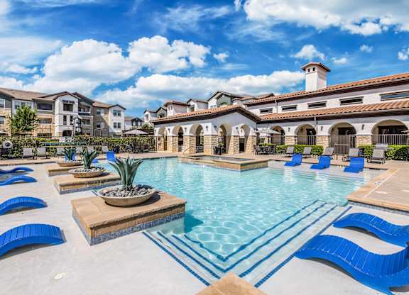 A large swimming pool with blue loungers and a building in the background.