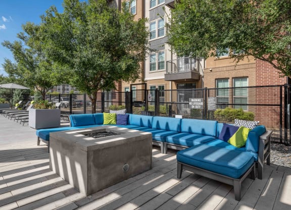 a firepit and lounge area on a wooden deck with a brick building in the background