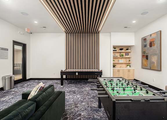 A foosball table is in the middle of a room with a green couch and a wooden bench.