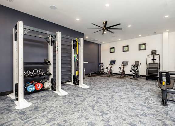 A gym with a variety of equipment including a squat rack, weight bench, and a fan.