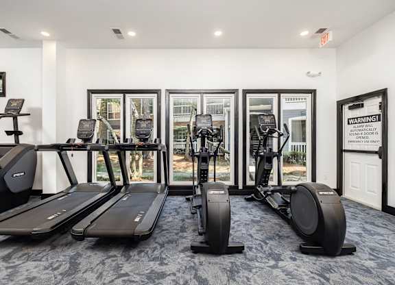 A gym with treadmills, elliptical machines, and a warning sign.