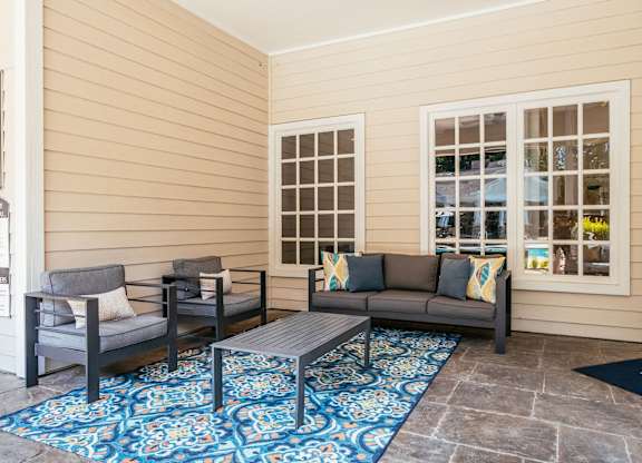 A patio with a couch, chairs, and a rug.