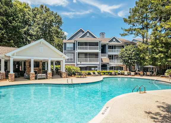 A large swimming pool in front of a house with a covered patio area.