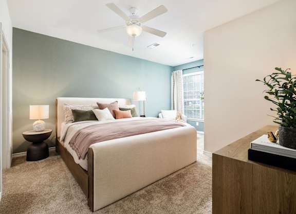 A bedroom with a bed, a ceiling fan, and a potted plant.