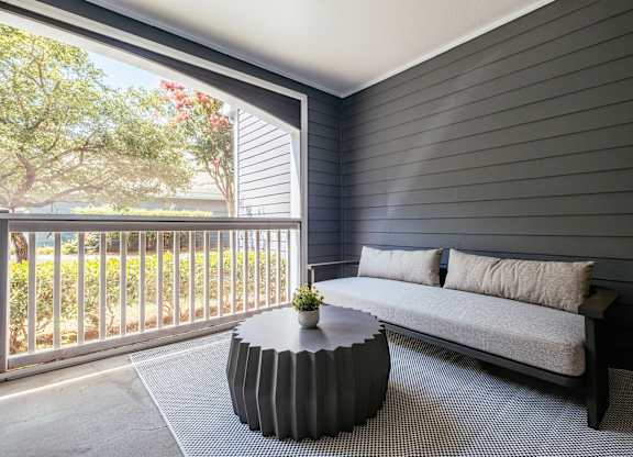A balcony with a white couch and a round table with a plant on it.