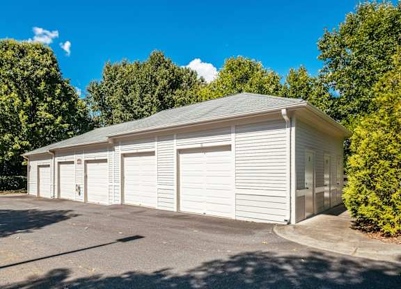 A two-car garage with a grey roof and white walls is surrounded by greenery.