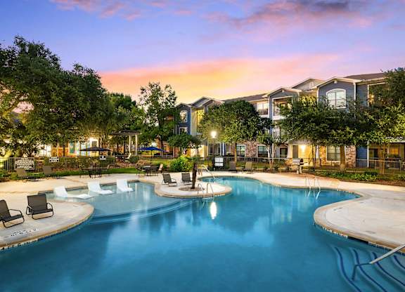 A swimming pool surrounded by lounge chairs and trees at dusk.