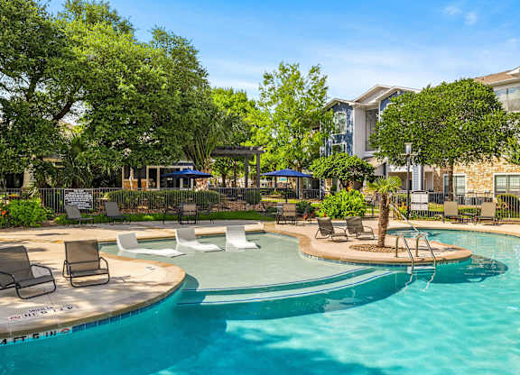 A swimming pool surrounded by chairs and trees.