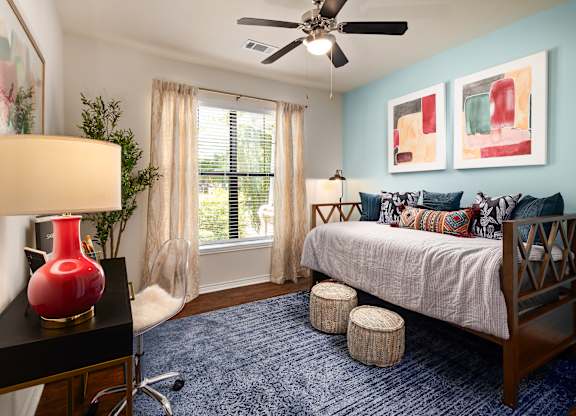 A bedroom with a bed, a ceiling fan, and a red vase on a table.