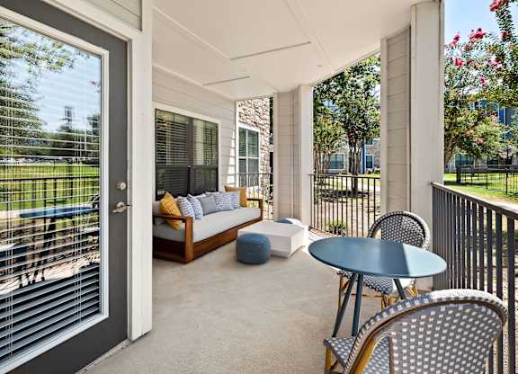 A balcony with a table and chairs overlooking a green area.