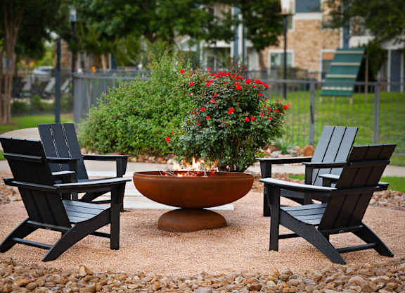 A fire pit surrounded by two chairs and a planter with red flowers.