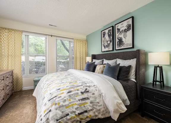 A bedroom with a bed, nightstand, and window with yellow curtains.