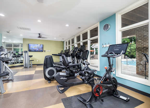 A gym with a row of stationary bikes and a television mounted on the wall.