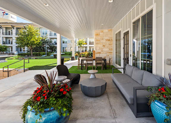 A patio with a grey couch, a table and a potted plant.