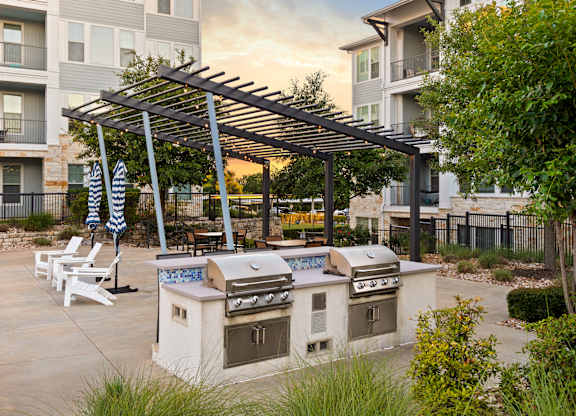 A patio with a grill and chairs under a pergola.