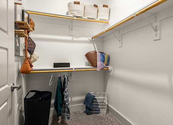 A small closet with a shelf and a black trash can.