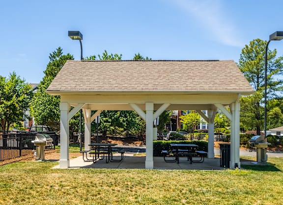 A white pavilion with a brown roof is surrounded by green grass.