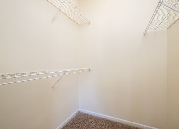 A white wall with a carpeted floor and a white ceiling fan.