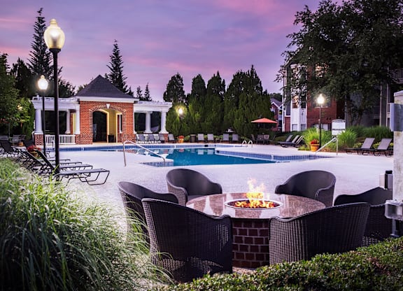 A poolside table with a fire pit in the middle of it.