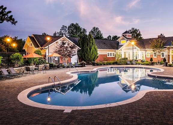 A large outdoor swimming pool surrounded by a brick patio and lounge chairs.