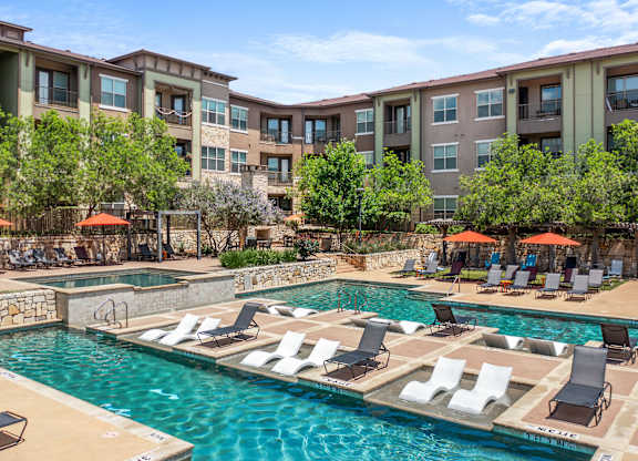 A large swimming pool with lounge chairs and umbrellas in front of apartment buildings.