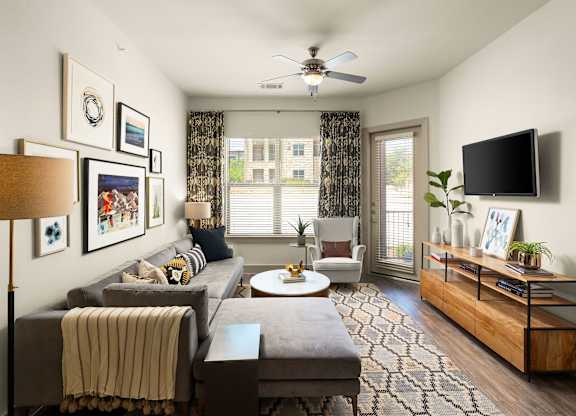 A living room with a grey couch, a coffee table, a television, and a ceiling fan.