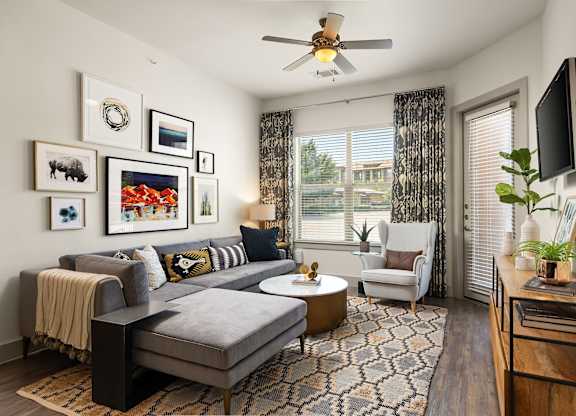 A living room with a grey couch, a coffee table, a television, and a ceiling fan.