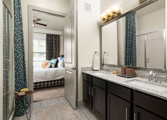 A bathroom with a mirror, sink, and a bedroom with a bed and a window.