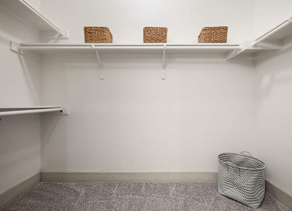 A white closet with three baskets on the shelf and a trash bag on the floor.