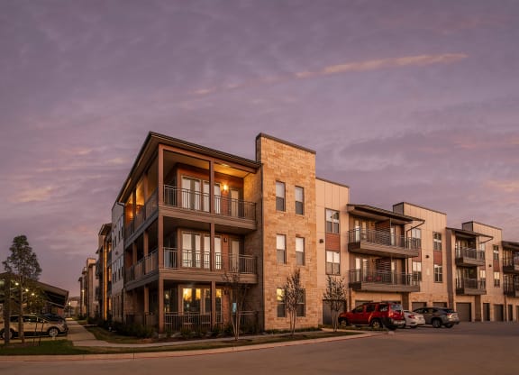 a rendering of a building at dusk with the lights on and cars parked in front of it