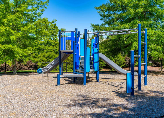 a playground with blue playset and slides in a park