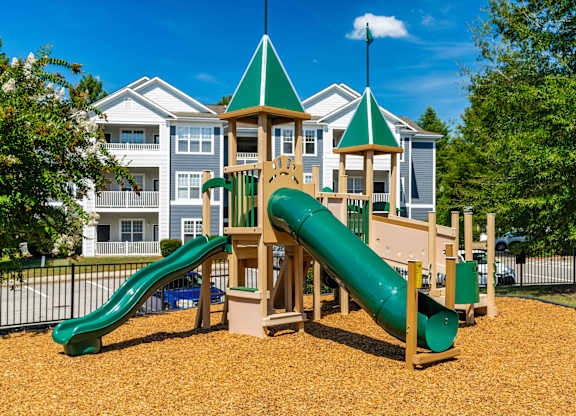 A playground with a green slide and a wooden play structure.