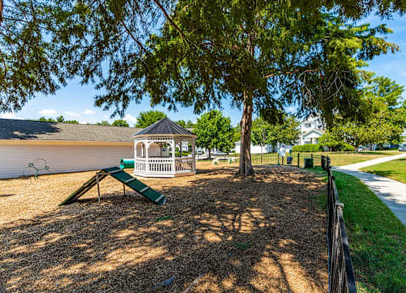 A playground with a green slide and a white gazebo.