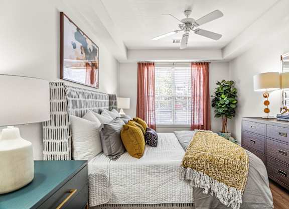 A bedroom with a bed, a ceiling fan, and a nightstand with a lamp.