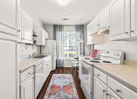 A kitchen with white cabinets and a red rug on the floor.