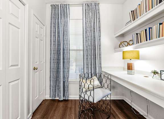 A room with a chair, a desk, and a window with curtains.
