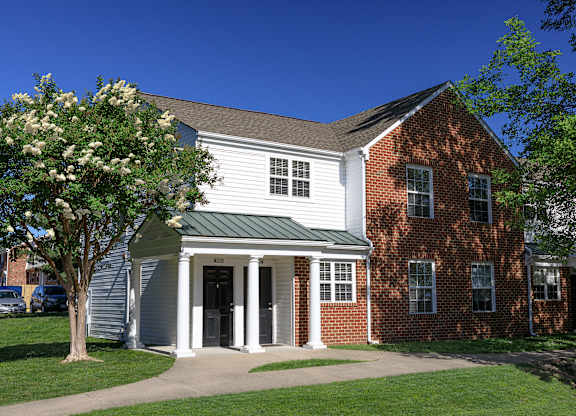 A white building with a green roof and a tree in front.