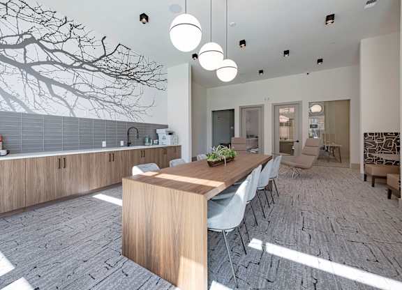a long wooden table with white chairs in a room with a tree mural on the wall