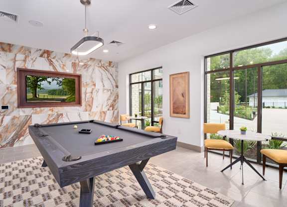 A pool table in a room with a marble wall and a painting of a landscape.