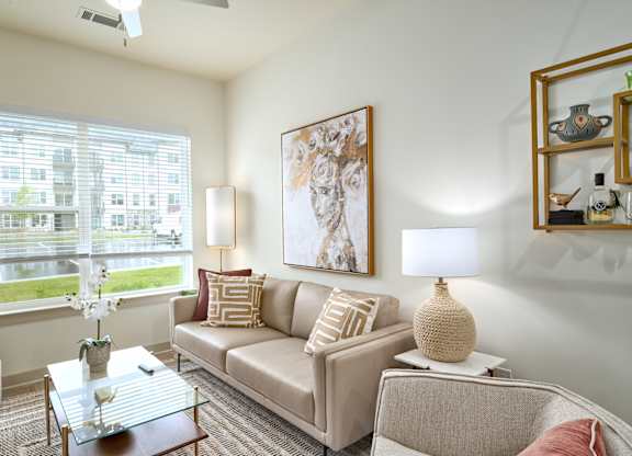 A living room with a beige couch, a glass coffee table, and a large painting on the wall.