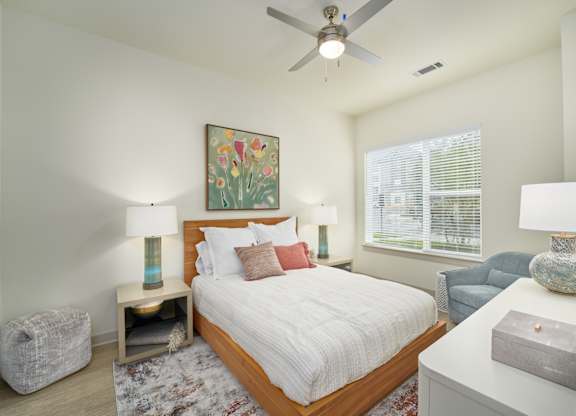 A bedroom with a large bed, a ceiling fan, and a painting on the wall.