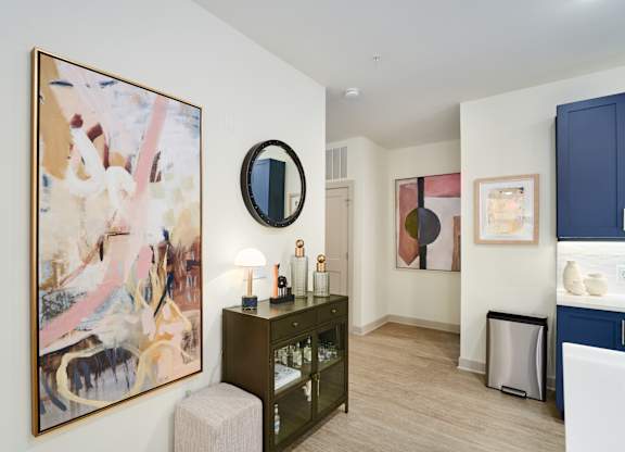 A living room with a painting on the wall and a mirror above a cabinet.